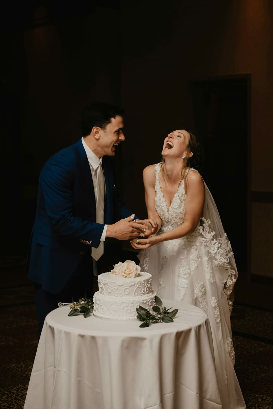 A couple laughing together as they cut a single-tier wedding cake.